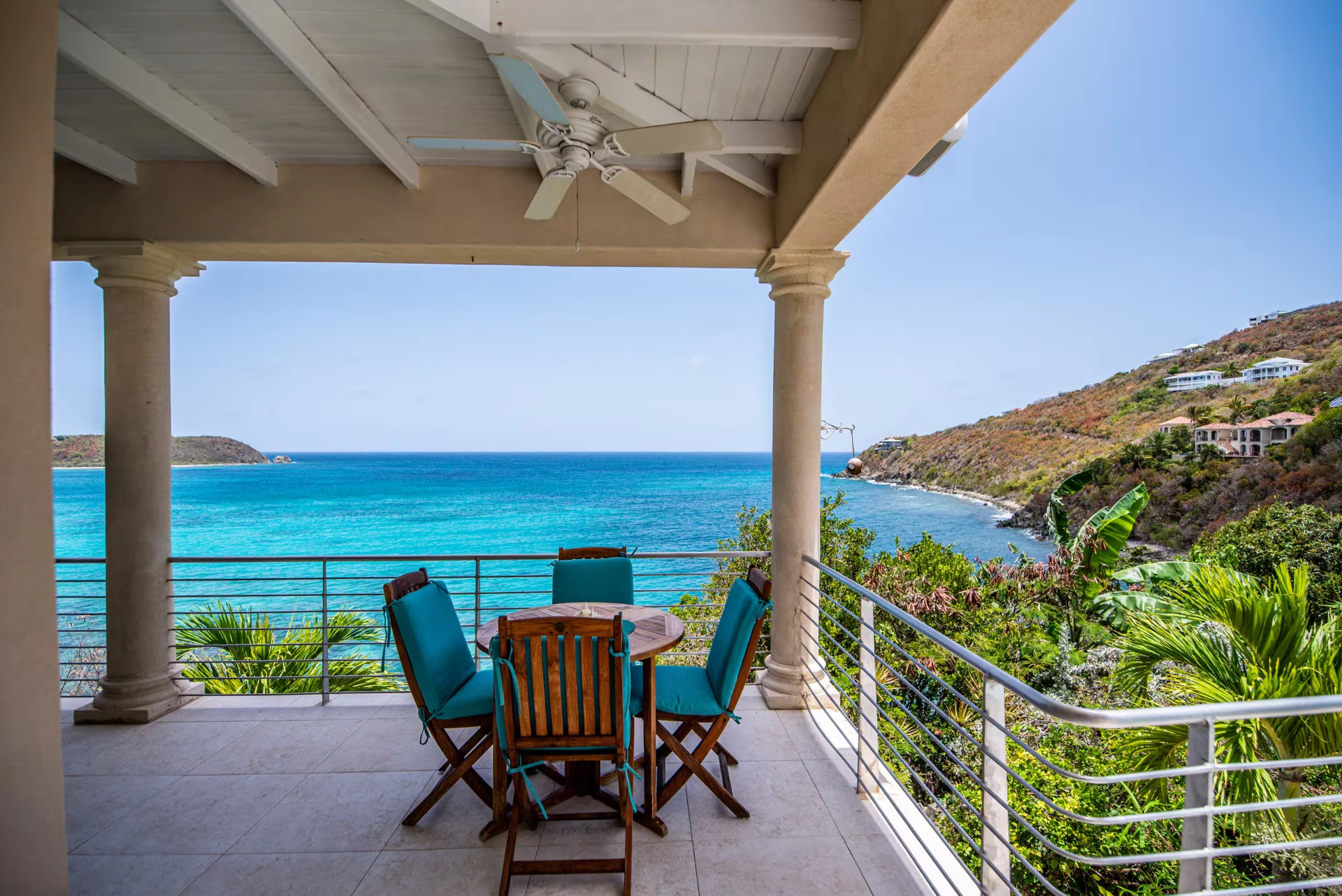 Covered balcony with teak table and chairs above the turquoise bay
