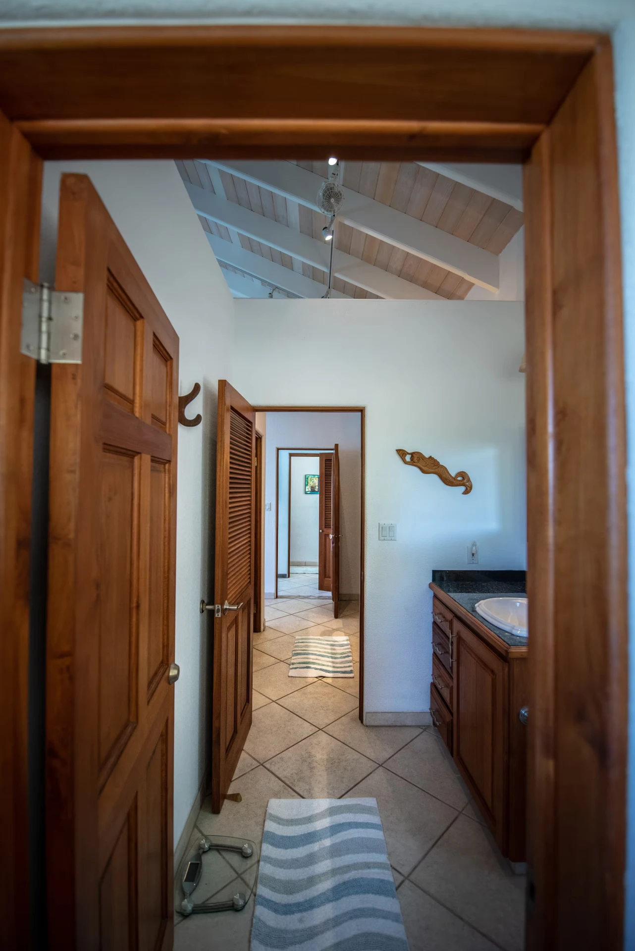 Hallway view of the shared downstairs bathroom with vaulted wood ceiling and granite vanity