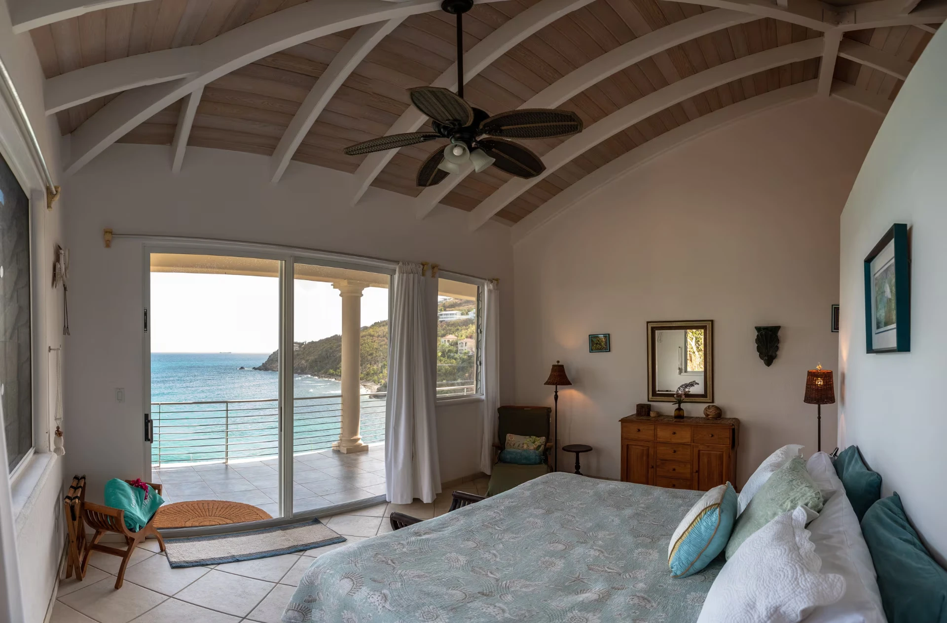 Master suite king bed under a vaulted wood ceiling with doors to a sea-view balcony