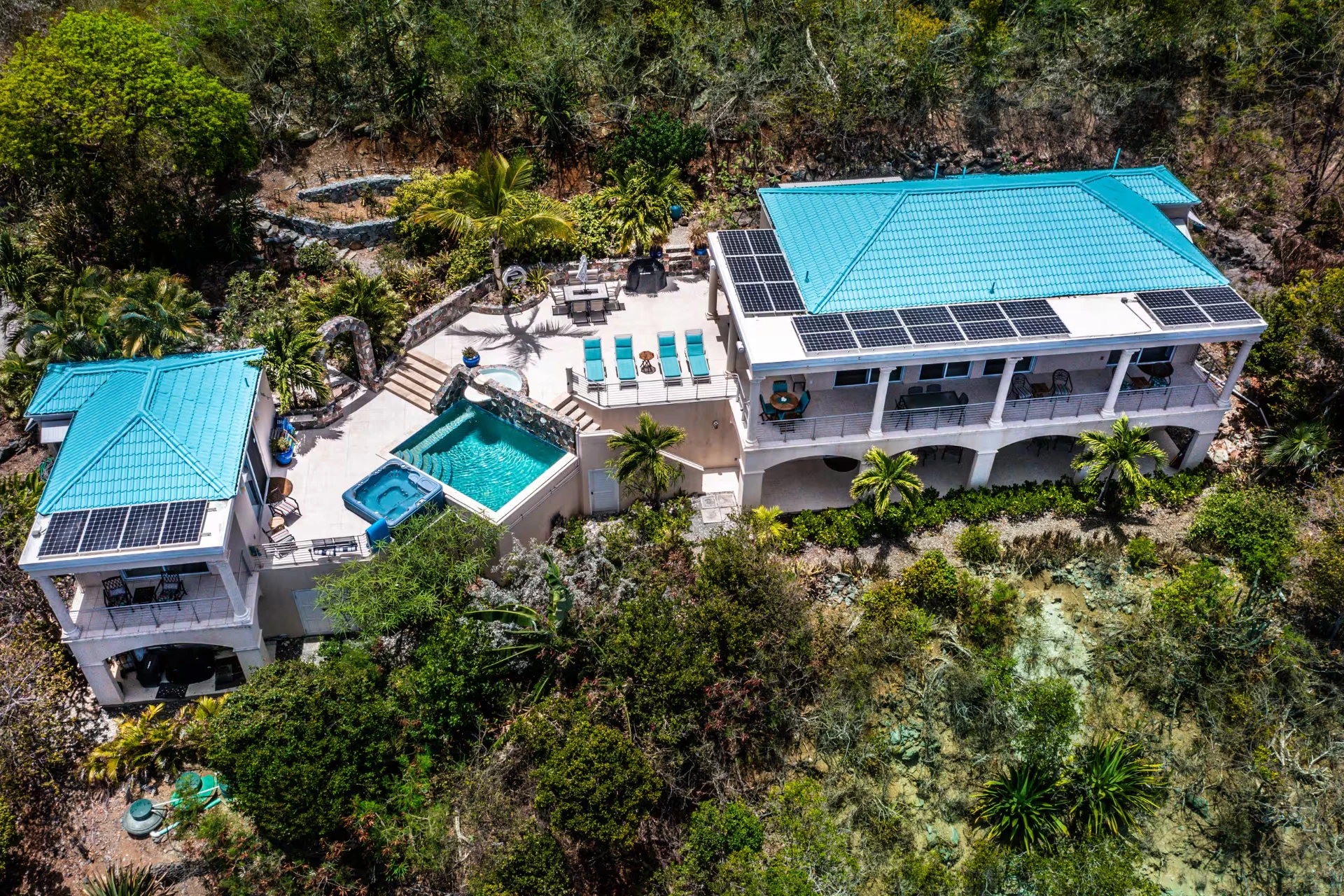 Aerial view of Sanctuary with its turquoise roofs, pool and hot tub above the coastline