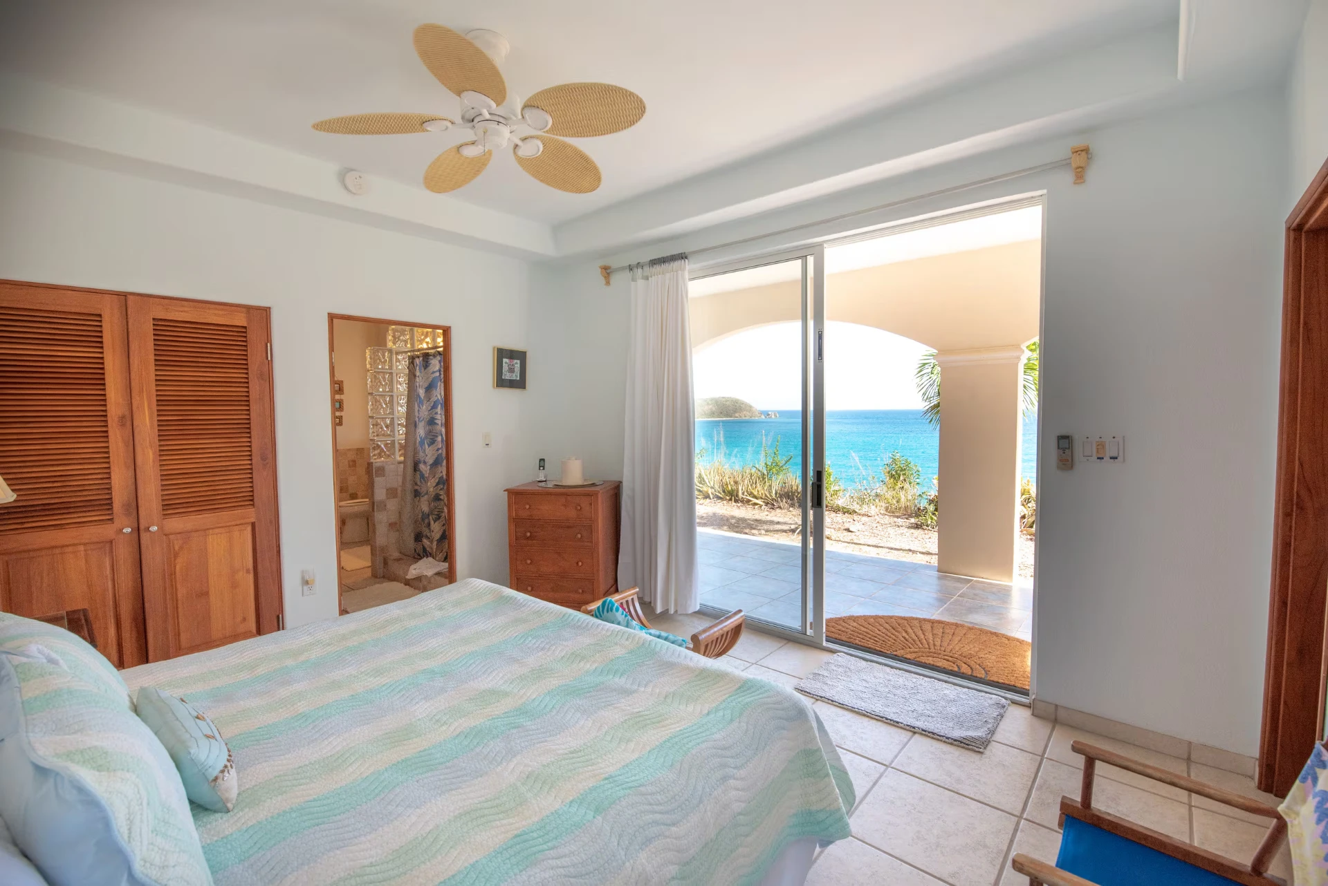 Downstairs king bedroom with sliding doors open to a private patio and the turquoise sea beyond